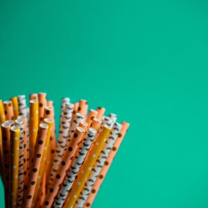 A bunch of colorful, biodegradable paper straws against a vibrant green background.