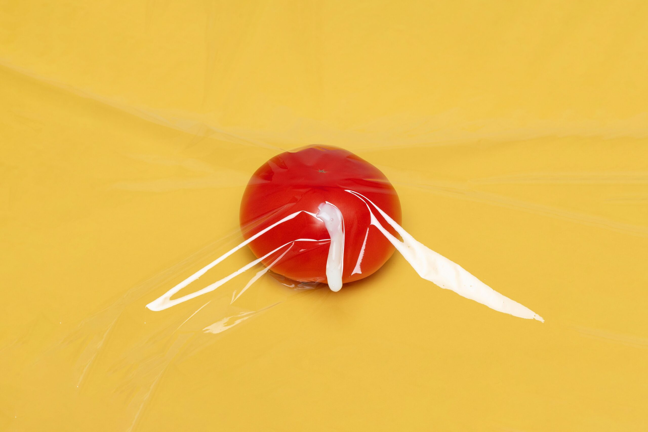 pexels photo 5751659 5751659 A fresh tomato wrapped in clear plastic wrap on a vibrant yellow background, highlighting freshness and packaging.