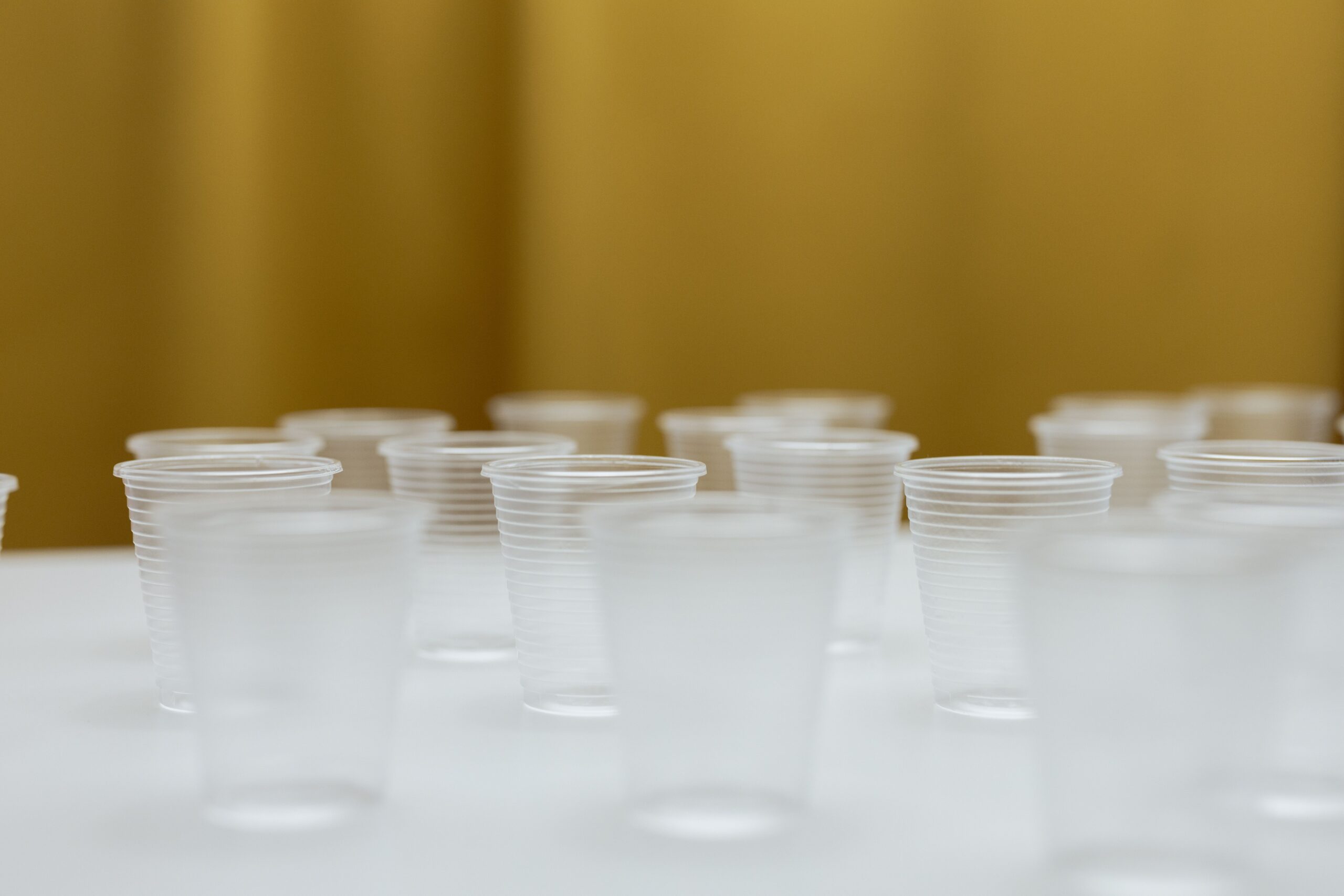 pexels photo 7829819 7829819 A collection of clear plastic cups arranged on a white table with a blurred background.